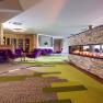 Moderne Hotellobby mit grün-braunem Teppichboden, Kamin, lila Sofas und Stühlen und Holztischen.