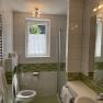 Modernes Badezimmer mit grünen Fliesen, Dusche, WC und Waschbecken.