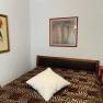 A bedroom with a bed, two framed pictures on the wall and a red bedside table.