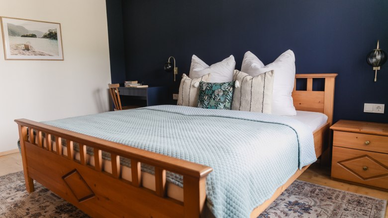 Gemütliches Schlafzimmer mit Holzbett, blauer Wand und dekorativen Kissen.