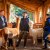 Three people stand in a wooden stable with alpacas.