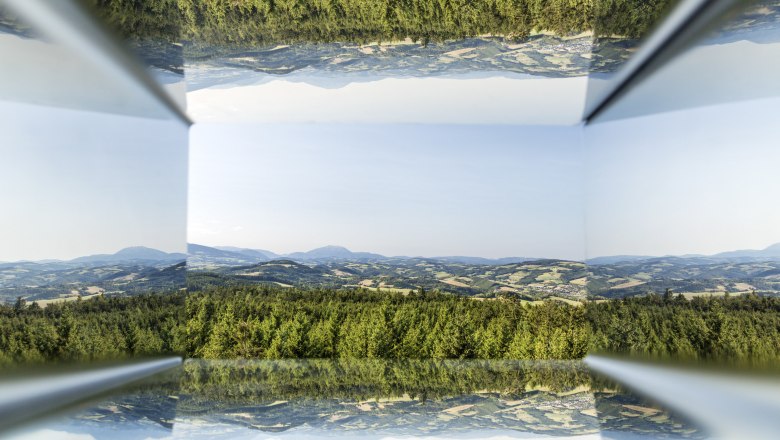 Spiegelung einer Landschaft mit Hügeln und Wäldern in einem prismatischen Objekt.