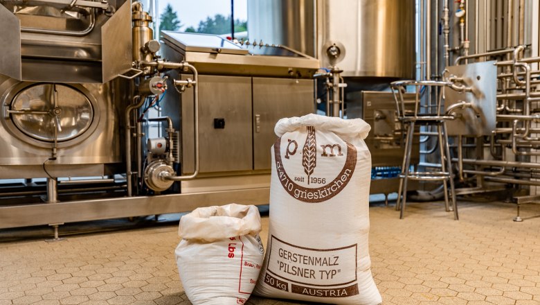 S&auml;cke mit Gerstenmalz in einer Brauerei vor Edelstahlmaschinen.