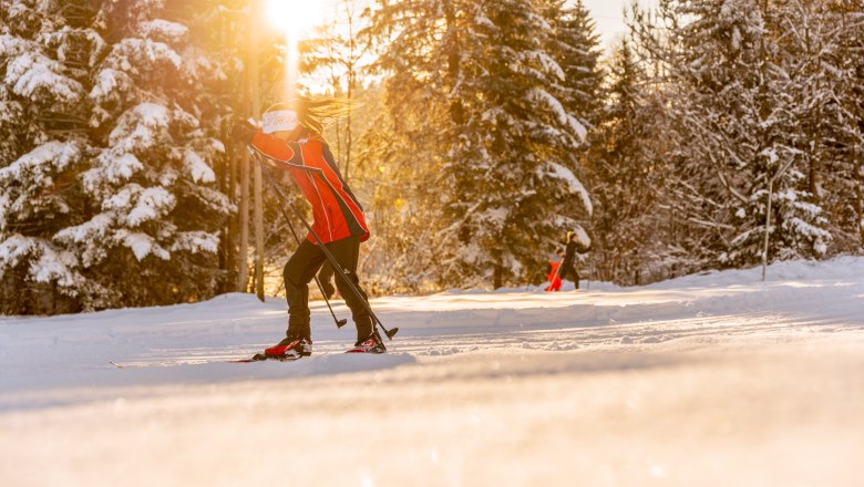 Langl&auml;ufer auf einer verschneiten Loipe bei Sonnenuntergang.