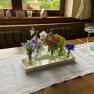 Ein Tisch mit einer weißen Tischdecke, dekoriert mit kleinen Vasen voller bunter Blumen und Kerzenhaltern.