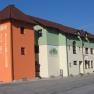 Ein Gasthof mit orangefarbenem Turm und grün-weißer Fassade an einer Straße.