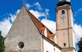 Wiesmath parish church with tower, stone cemetery wall and clock against a blue sky.