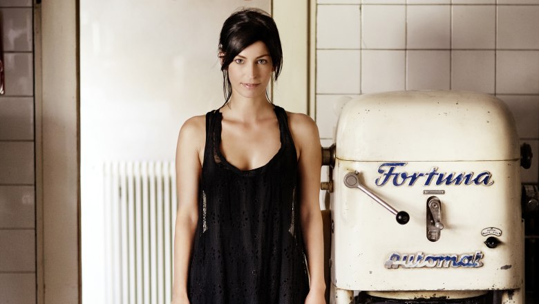 Eine Frau in einem schwarzen Kleid steht neben einer alten B&auml;ckereimaschine mit der Aufschrift 'Fortuna'.