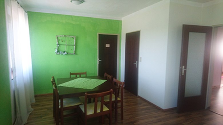 Dining area with green-painted wall, wooden table and chairs.