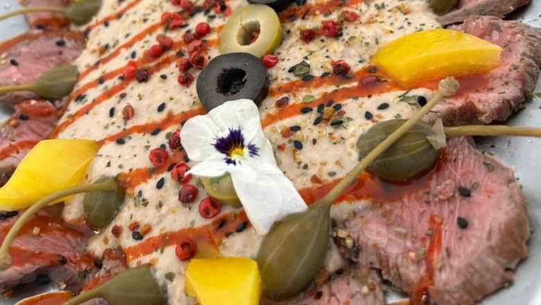 Nahaufnahme eines dekorativen Tellers mit rosa, feingeschnittenem Fleisch mit Kapern, Oliven und essbaren Bl&uuml;ten.