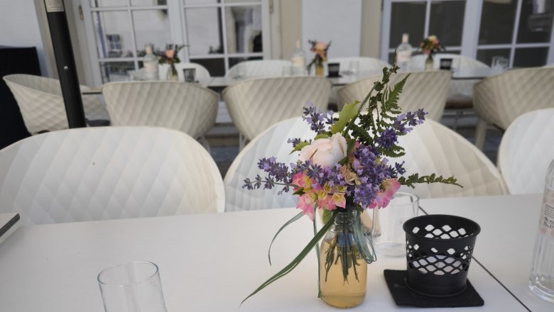 Gedeckter Tisch auf einer Terrasse mit Blumenstrau&szlig; und Besteck.