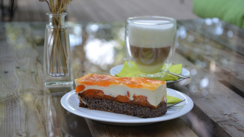 Teller mit Obstkuchen auf Holztisch, im Hintergrund ein Glas mit Kaffee und eine Vase.