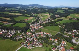 Luftaufnahme von Zöbern, einer ländlichen Gemeinde mit Häusern und Feldern, umgeben von Hügeln und Wäldern.