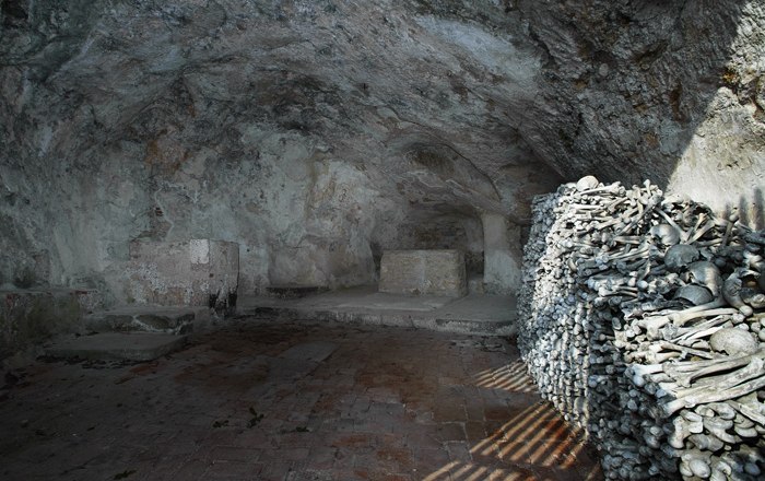 Interior view of a cave church with a pile of bones on the wall.