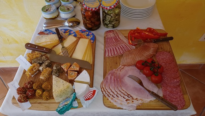 Breakfast buffet with cheese, cold cuts, tomatoes and peppers on wooden boards.