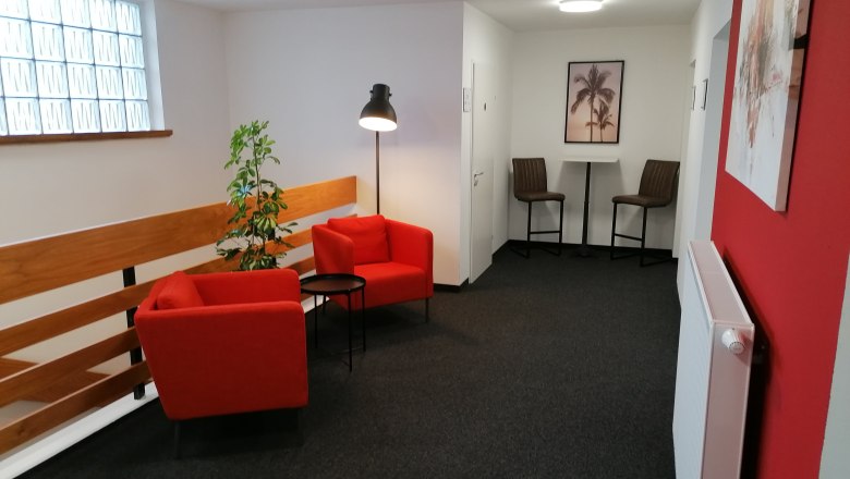 Cozy sitting area with red armchairs and floor lamp in a hallway.