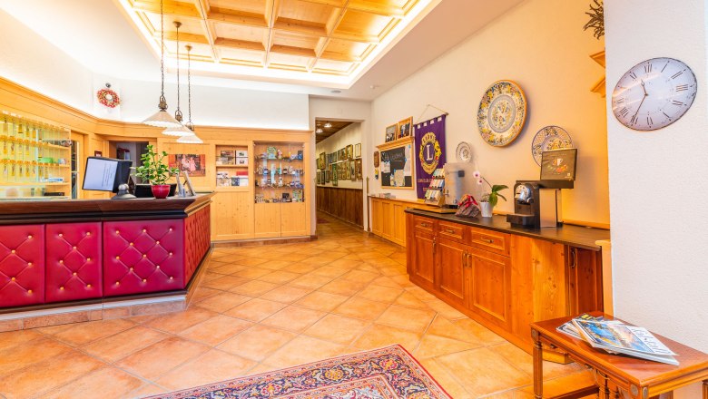 Reception area with wooden furniture, red counter, decorative plates on the wall and a clock.