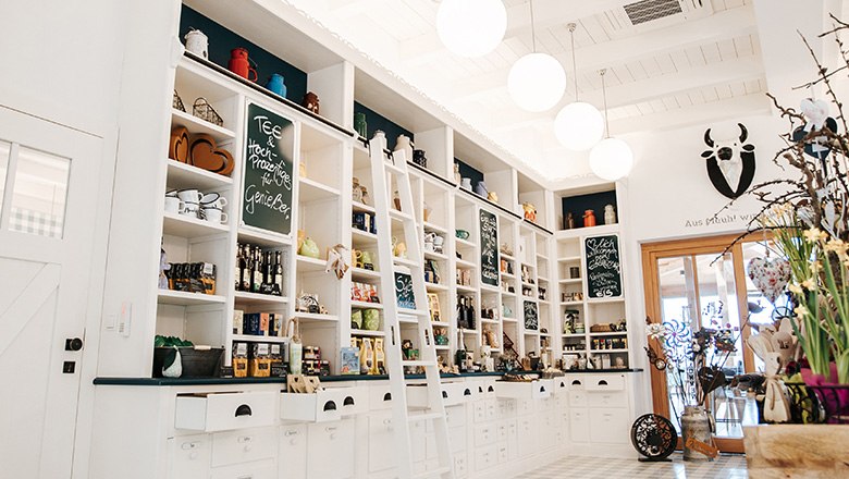 Hofladen mit wei&szlig;en Regalw&auml;nden gef&uuml;llt mit diversen Produkten, daneben Dekoration.