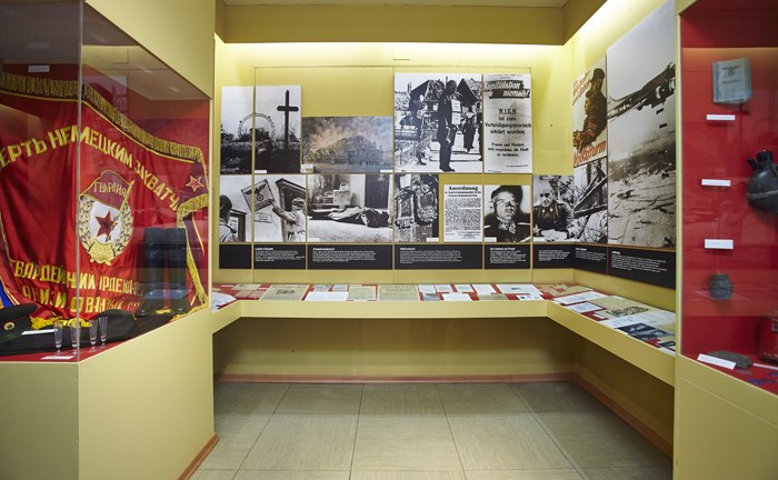 Exhibition room with historical photos, documents and a red flag.