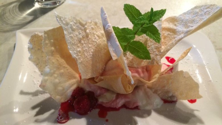 Ein Dessert mit Himbeeren, dünnen Teigblatten und Minze auf einem weißen teller angereichtet.