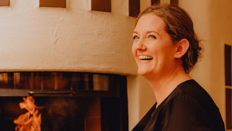 Woman smiling in front of a fireplace with a burning fire.