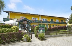 Gelbes Gebäude mit Balkon und Blumen, Krumbacherhof, Eingang mit Vordach und Schildern.