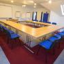 Konferenzraum mit U-förmigem Tisch und blauen Stühlen.