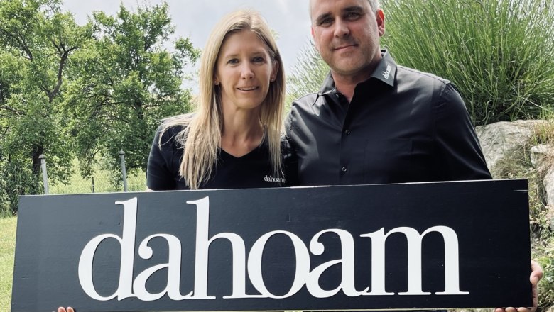 Zwei Personen halten ein Schild mit der Aufschrift 'dahoam' im Freien.