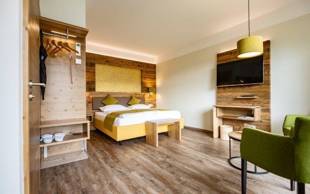 Modern hotel room with wooden furniture, double bed, green armchair and flat screen TV.