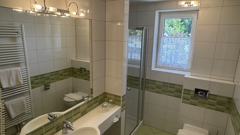 Modernes Badezimmer mit grünen Fliesen, Dusche, Waschbecken und WC.