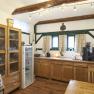 A cozy breakfast room with wooden furniture, a fridge, a coffee machine and decorative wooden beams on the ceiling.