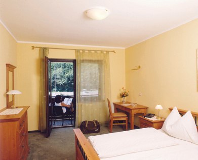 A cozy hotel room with double bed, desk, chest of drawers and balcony with a view of the greenery.