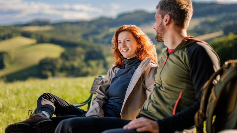 Zwei Personen sitzen auf einer Bank in einer gr&uuml;nen Landschaft.