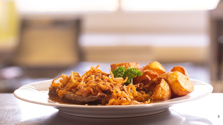 Ein Teller mit Zwiebelrostbraten, R&ouml;stzwiebeln und Bratkartoffeln.