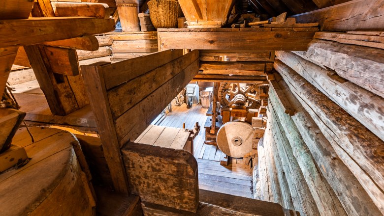Interior view of an old mill with wooden structures and millstone.