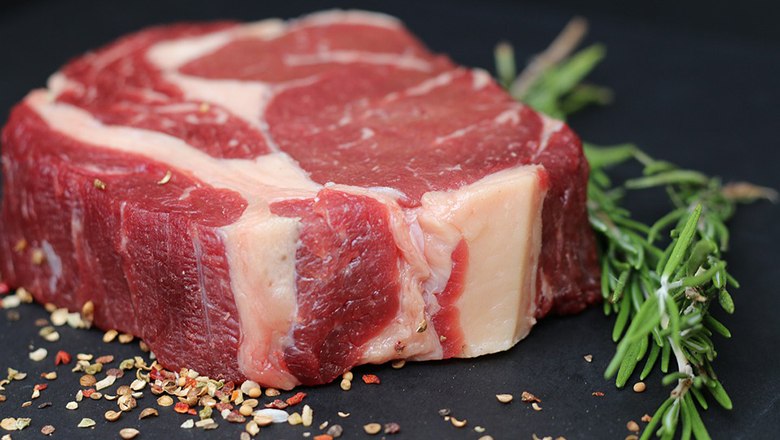 Ein rohes Steak auf einer dunklen Platte mit Gewürzen und Kräutern dekoriert.