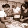 Three people in traditional dress prepare food in a kitchen.