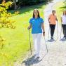 Drei Personen beim Nordic Walking auf einem Kiesweg in einem gr&uuml;nen Park. Eine der Personen ist eine Trainerin des Gesundheitsresorts K&ouml;nigsberg.
