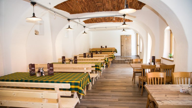 Traditioneller Innenraum eines Gasthauses mit Holztischen und karierten Tischdecken.