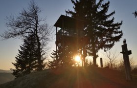 Sonnenuntergang hinter einem Aussichtsturm und Bäumen.