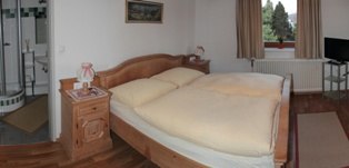 Gemütliches Gästezimmer mit Doppelbett, Nachttisch und Fenster mit Vorhängen.