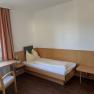 Ein einfaches Hotelzimmer mit Einzelbett, Tisch, Stuhl und Fenster mit Vorhängen.