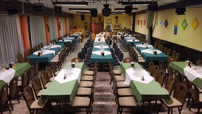 Ein gro&szlig;er Saal mit langen, gedeckten Tischen und St&uuml;hlen, bereit f&uuml;r eine Veranstaltung.