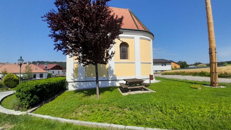 Round church with yellow façade, surrounded by green meadow and trees, in sunny weather.