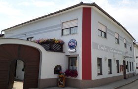 Außenansicht Café Sabine mit Holztor, weiß-roter Fassade und Aufschrift "Café-Restaurant".