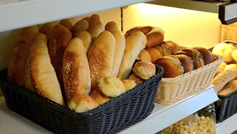 Regal mit verschiedenen Brotsorten in Körben, darunter Baguettes und Brötchen.