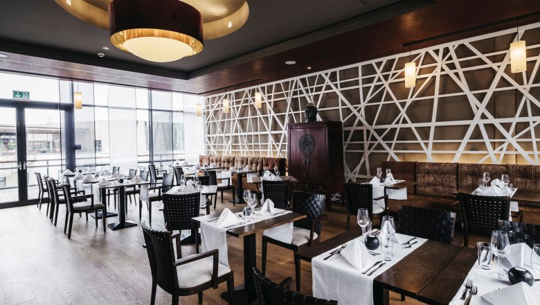 Elegantes Restaurant mit modernen asiatischen Designelementen, gedeckten Tischen und großen Fenstern.