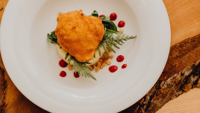 Ein gebackenes Ei auf einem Teller mit P&uuml;ree und roten Tupfen.