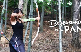 A woman shoots with a bow in the forest. The text "Bogenschiaßn in da Pampa" is superimposed.