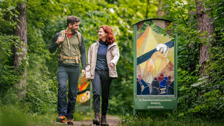 Ein Paar wandert auf einem Waldweg neben einer bunten Glasinstallation.